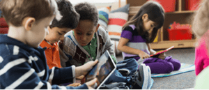 Young children learning together on tablets in a classroom.